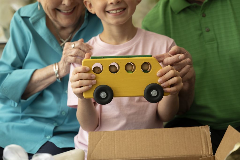 Child holding yellow wooden school bus that was made by the Emerald Heights wood working crew