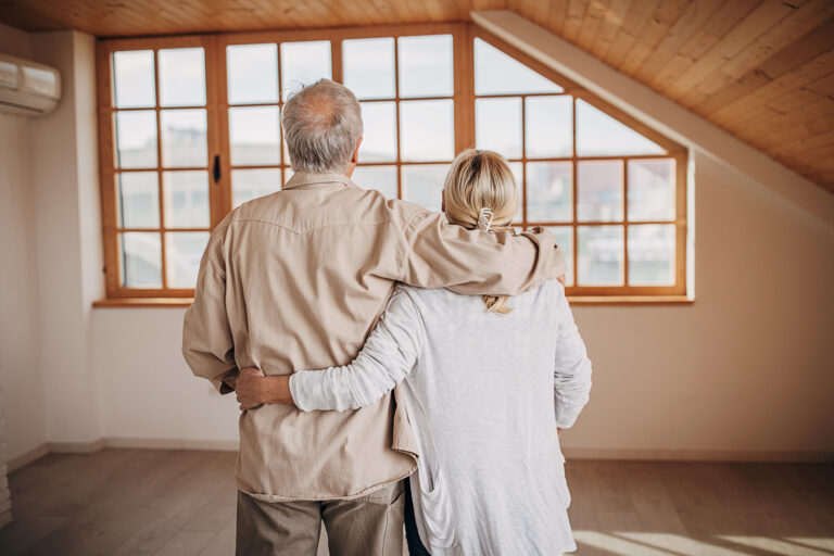 Older couple standing together and looking out a window, reflecting on their next chapter